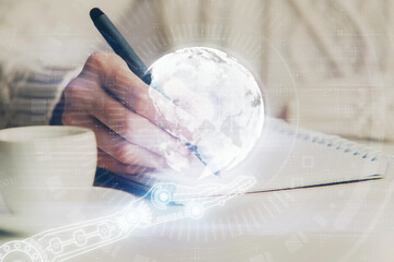 Double exposure of hands making notes with world map hologram and data theme icons. Concept of global computer data.