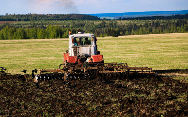  tractor plows and harrows  land in  large field on  sunny spring day. preparing  soil for planting crops, plowing  soil with  tractor with  disk plow.