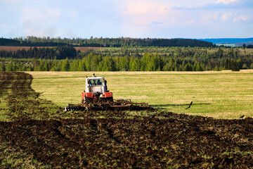 Fototapeta premium tractor plows and harrows land in large field on sunny spring day. preparing soil for planting crops, plowing soil with tractor with disk plow.