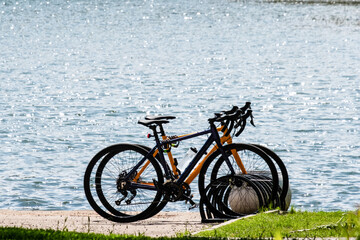 A pair of bicycles parked on the shore of a reservoir on a summer sunny day without people. The surface of the water shines in the sun. The concept of outdoor activities.