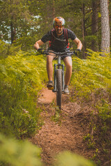 Fototapeta na wymiar Man riding downhill with a mountain bike towards camera in a lush green environment on a dirt single track course. Tall man going downhill with a bike.