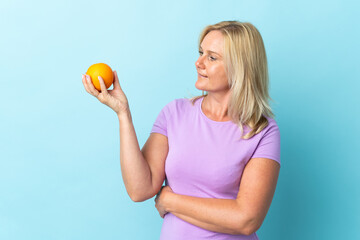 Middle age Lithuanian woman isolated on blue background holding an orange