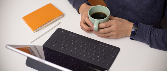 Female employee holding coffee cup while reading informations on digital tablet