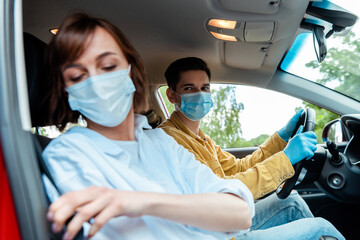 Fototapeta na wymiar man and woman in medical masks and protection gloves sitting in car during coronavirus pandemic, selective focus