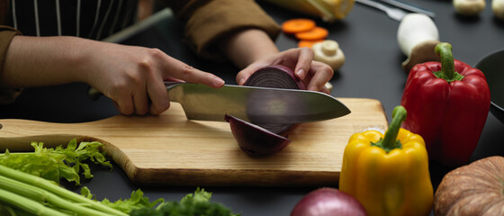 Side view of female cook cutting fresh red onion on chopping block