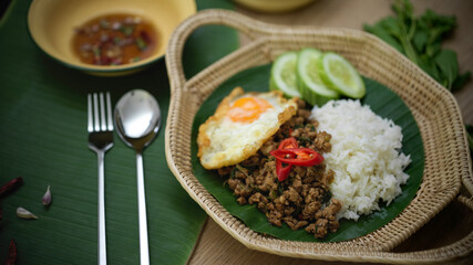 Stir fried minced pork with basil (Pad ka prao), rice fried egg serving on wicker plate and silverware