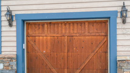 Panorama Brown wood garage door with blue frame flaned by wall mounted vintage lanterns