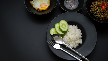 Stir fried minced pork with basil (Pad ka prao), rice, fried egg and chili fish sauce on black dinning table with copy space