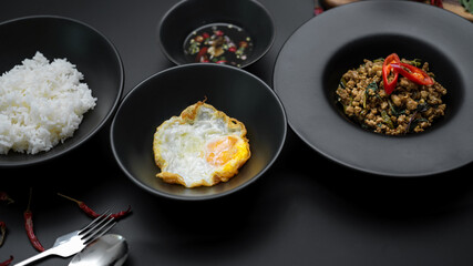Stir fried minced pork with basil (Pad ka prao), rice, fried egg and chili fish sauce serving on black ceramic plates in Thai restaurant