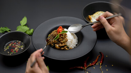 Female eating Stir fried minced pork with basil (Pad ka prao) on black table in Thai restaurant