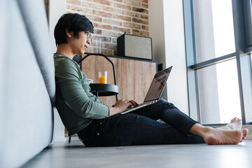 Image of focused asian man working with laptop while sitting