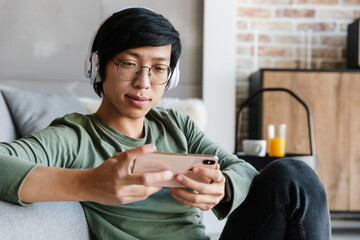 Image of young asian man using cellphone and wireless headphones