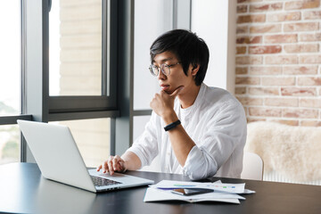 Image of focused asian man working with laptop and documents