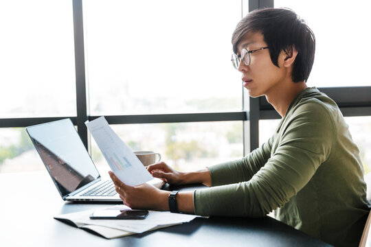 Image of focused asian man working with laptop and documents