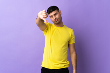 Young Colombian man isolated on purple background showing thumb down with negative expression