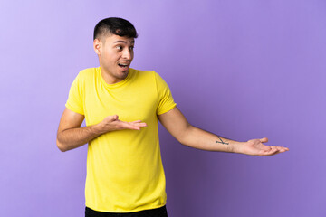 Young Colombian man isolated on purple background with surprise expression while looking side