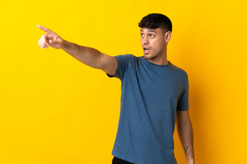 Young Colombian man isolated on yellow background pointing away