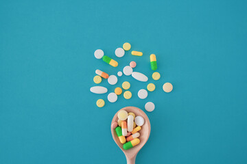 Colorful pills and capsules on a wooden spoon on a blue background,  pills are scattered in the center from bottom to top, isolated