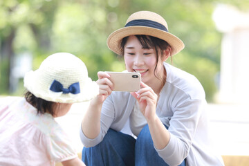 砂場で遊ぶ子供をスマートフォンで撮影する母親
