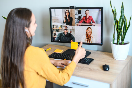 Video call, video meeting with colleagues, coworkers. A young woman watches on PC display with a multiracial people on it and showing thumbs up. Good connection