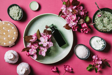 Obraz na płótnie Canvas Set of natural skin care products and pink flowers in a green plate and black bowls on a pink background. Spa treatment concept.