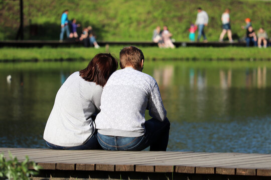 Love couple sitting on a lake coast in a park. Summer leisure, romantic date on a nature