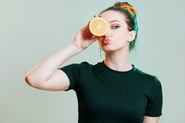 portrait of a beautiful young woman with bun hairstyle and elegantly sandwiched orange fruit between hands,fashion portrait on studio backgrond with green light