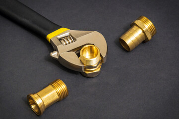 Plumbing brass fittings and adjustable spanner closeup on dark background during repair or...