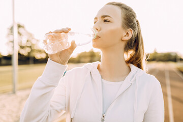 Athletic beautiful runner drinks water from a plastic bottle after running. A girl quenches her thirst after outdoor fitness classes