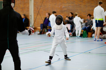 Little kid boy fencing on a fence competition. Child in white fencer uniform with mask and sabre....