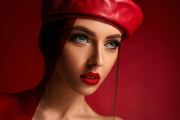 Beauty fashion portrait of woman in red leather beret in studio on red background. girl with luxurious make-up. copy space