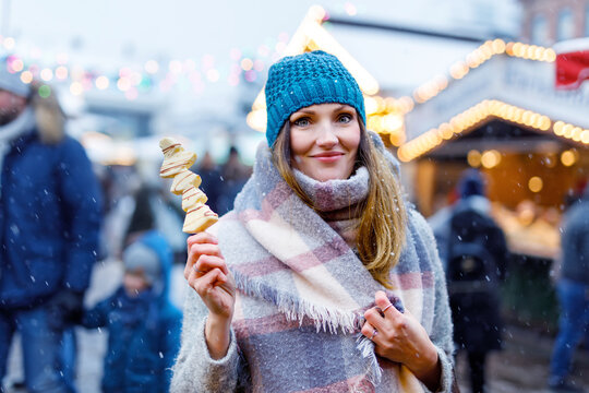 Beautiful young woman eating white chocolate covered fruits on skewer on traditional German Christmas market