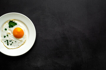 Fried eggs on plate - black background top-down copy space