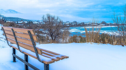 Naklejka premium Panorama Empty outdoor bench on snowy terrain overlooking frozen Utah Lake in winter