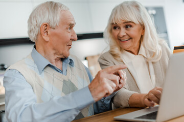 smiling elderly couple pointing shopping online with credit card and laptop at home during self isolation