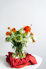 Stack of neatly folded vintage-printed summer dresses. Summer lifestyle, capsule wardrobe. Bouquet of bright ranunculus.