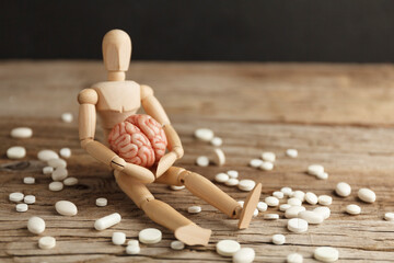 Toy man holds brain in his hands, sits next to pills. Treatment of headache and depression. Drug...
