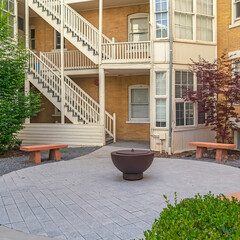 Square Fire pit with stone benches against building with yellow brick wall and stairs