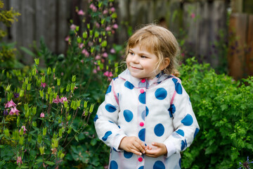 Outdoor portrait of happy smiling little toddler girl wearing rain jacket on rainy cloudy day. Cute healthy child in colorful clothes outdoor activity