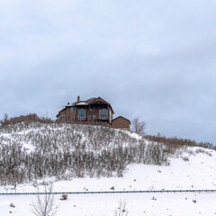 Square Home on top of a hill with leafless plants and fresh snow on the slope in winter