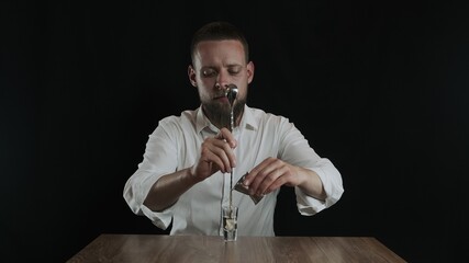 The bartender pours irish cream from jigger to cocktail glass with sambuca