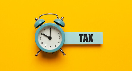 Clock with a reminder of the payment of taxes on a yellow background, financial statements.