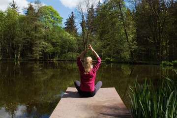 Fototapeta na wymiar Young woman sitting on dock on lake meditating. Self-isolation in the open air