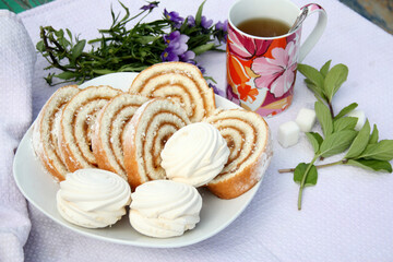   biscuit roll, marshmallows, a tea mug, mint leaves and a bunch of flowers on a light background. Afternoon Tea
