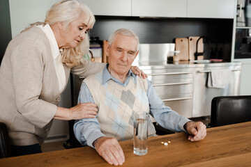 elderly wife and ill husband with pills and glass of water at home on quarantine