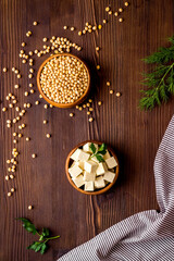 Tofu cubes in bowl and soybeans on wooden kitchen table top-down