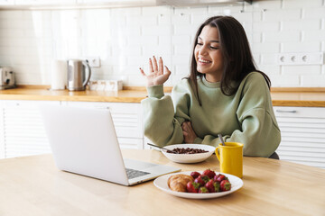 Photo of woman waving hand and using laptop while having breakfast