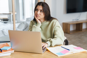 Photo of perplexed student woman using laptop while doing homework