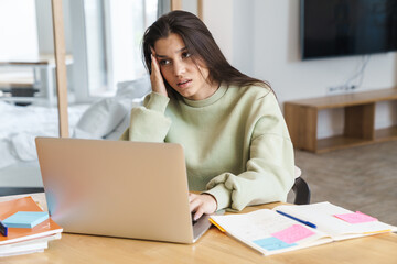 Photo of student with headache woman using laptop while doing homework