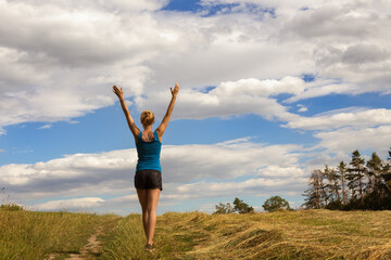 Fototapeta premium young woman walking alone in the field and enjoying nature with arms wide open.